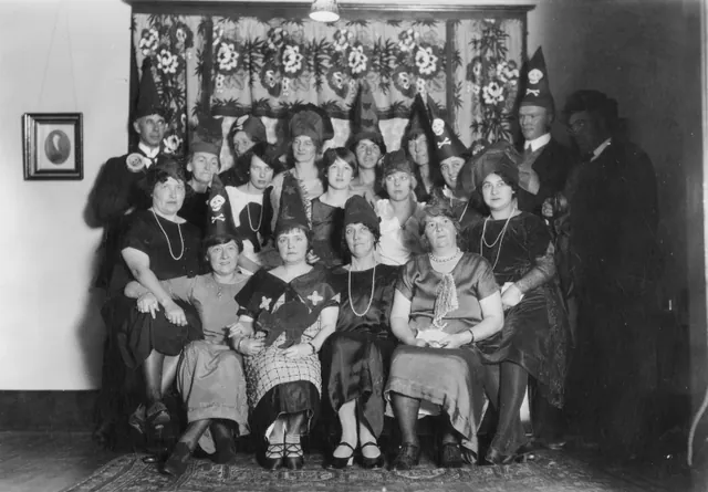 Guests in pointed witch hats with skull badges at a Halloween party in Wainwright in the 1920s
